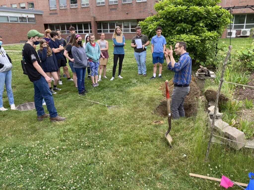 Keith Zaltzberg-Drezdahl in a knee-deep hole demonstrating soil health concepts to onlooking participants